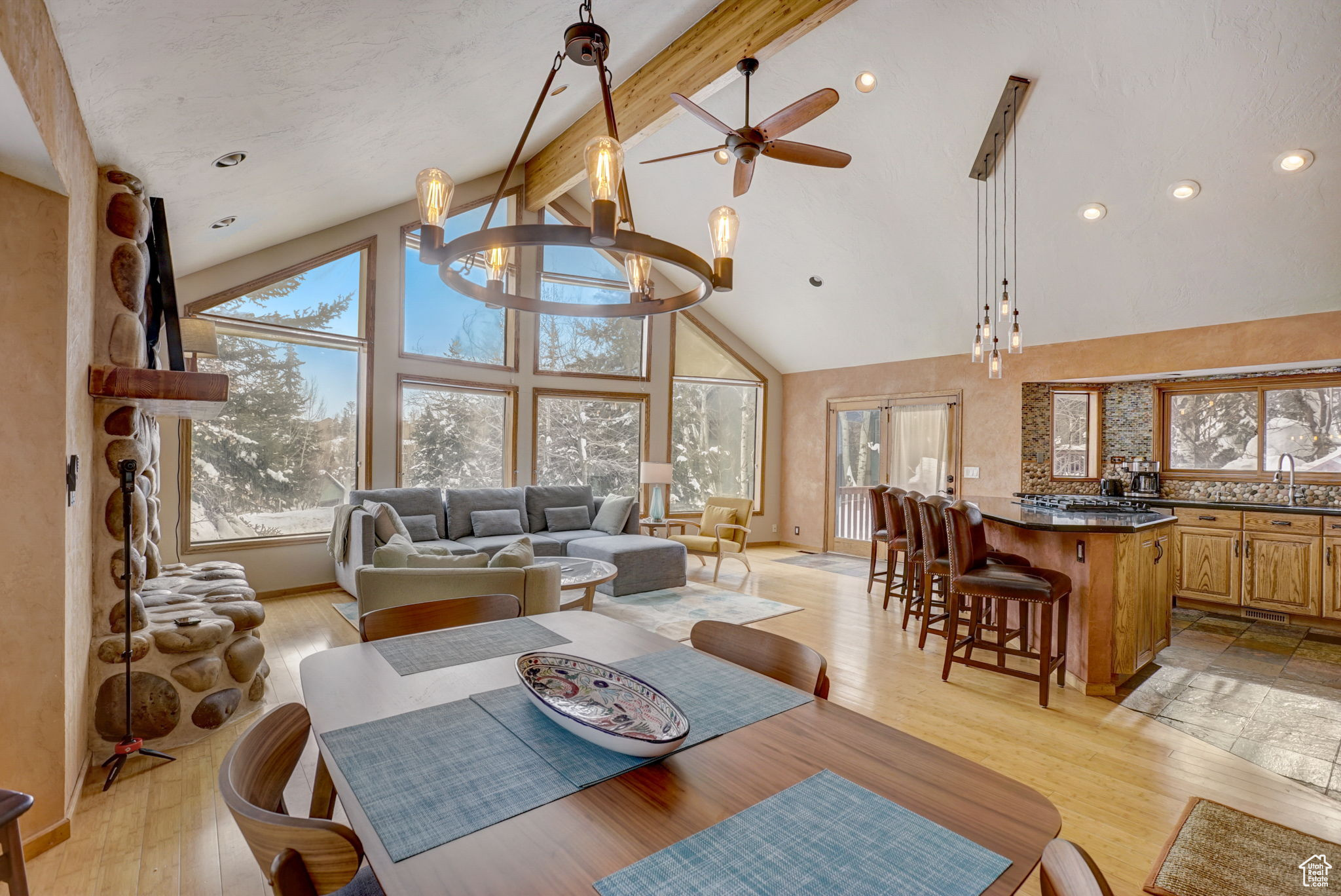 Dining area featuring high vaulted ceiling, ceiling fan with notable chandelier, beam ceiling, and light hardwood / wood-style flooring