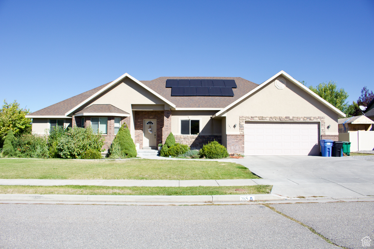 View of front facade featuring a garage, solar panels, and a front lawn