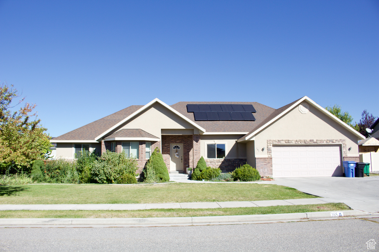 View of front facade featuring a garage, solar panels, and a front yard