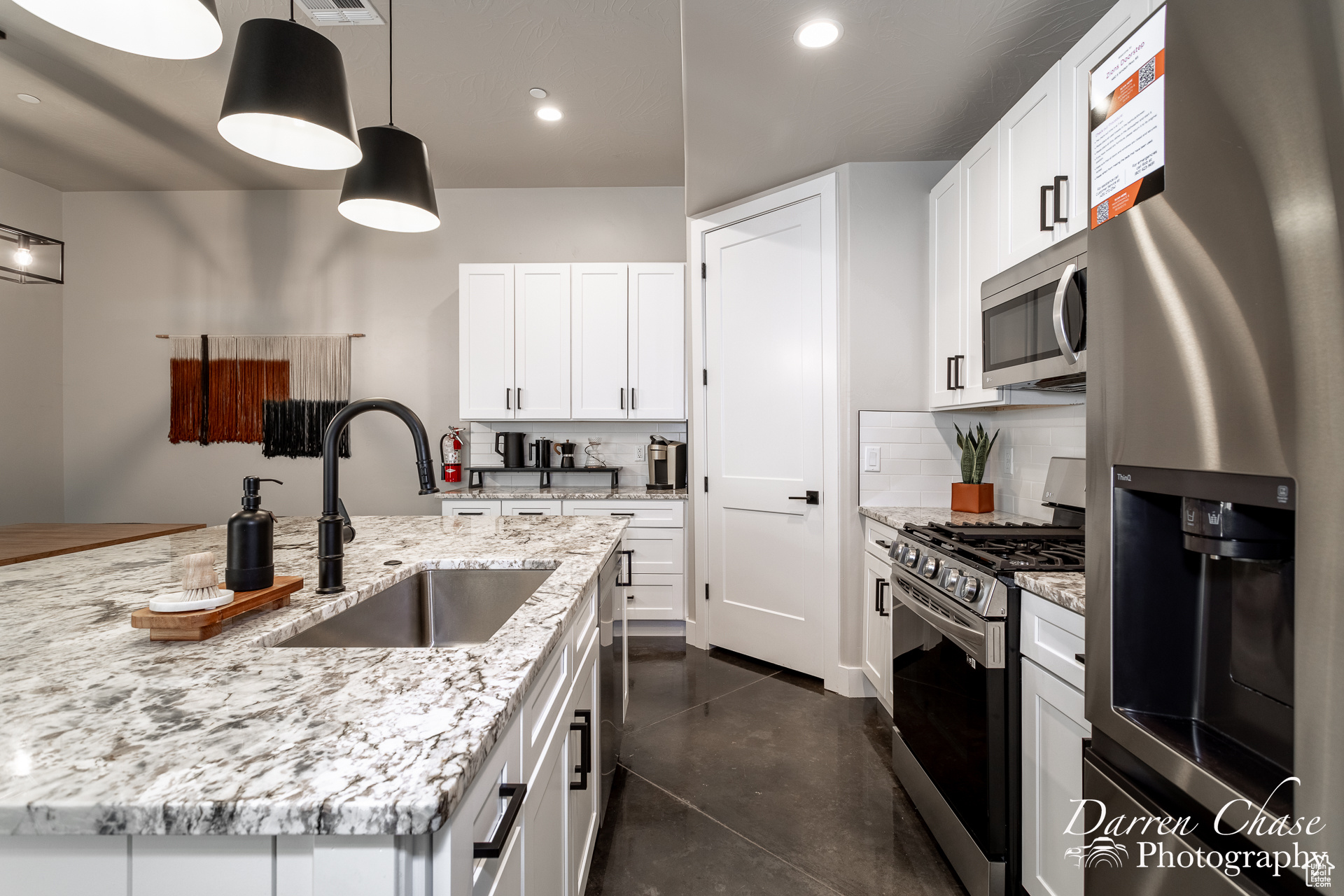 Kitchen with hanging light fixtures, white cabinetry, backsplash, stainless steel appliances, and sink