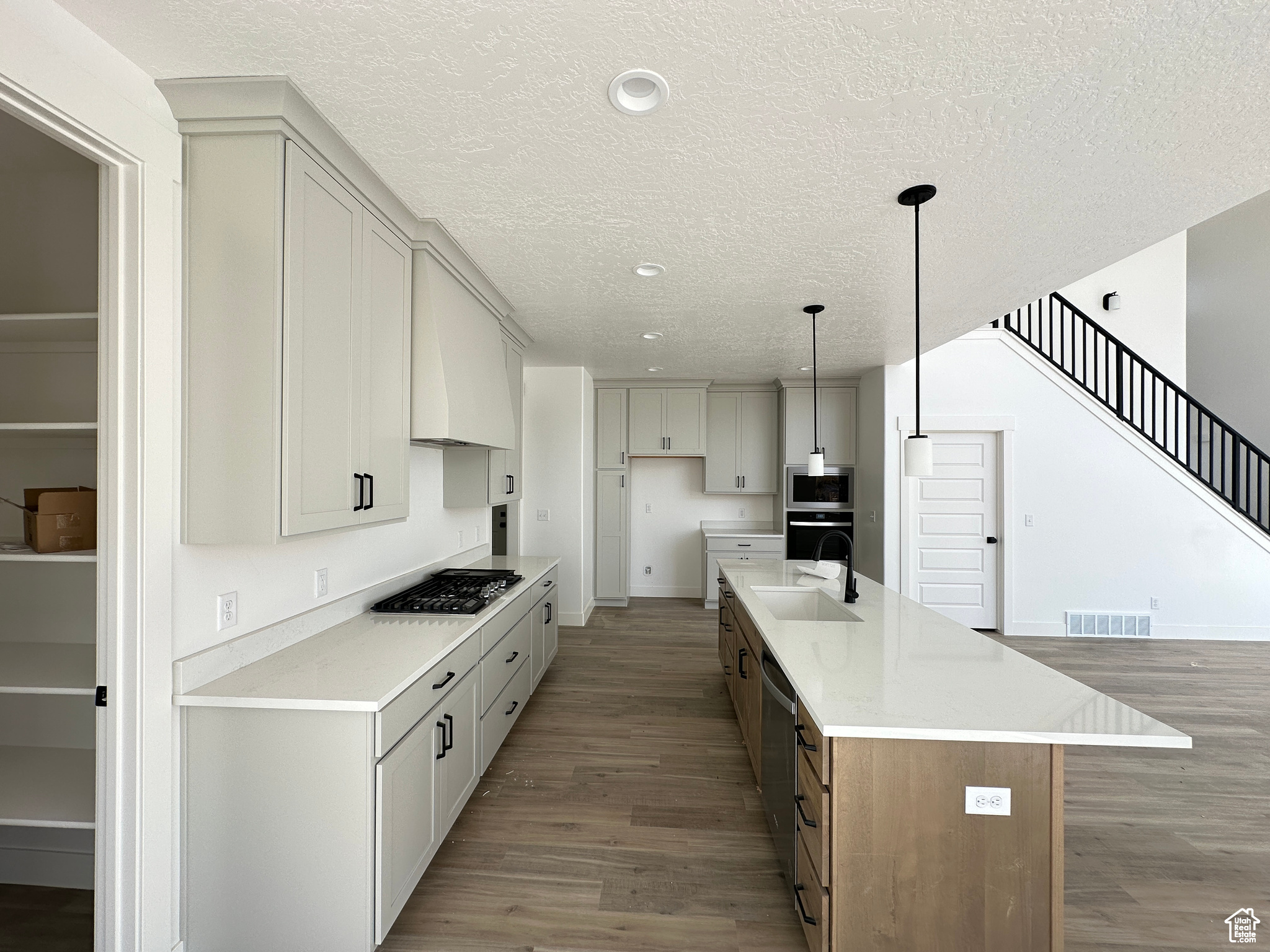 Kitchen with an island with sink, hanging light fixtures, sink, dark wood-type flooring, and stainless steel appliances