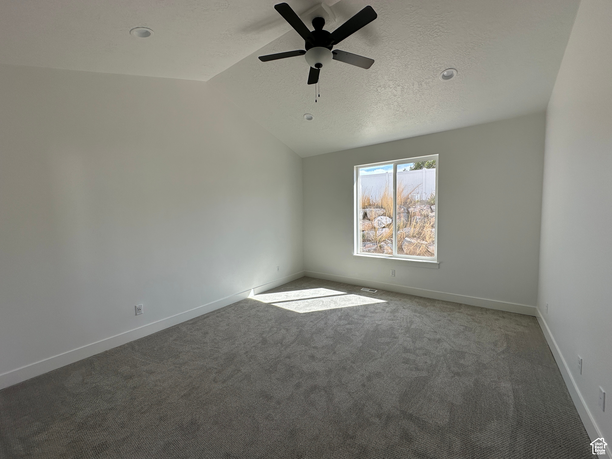 Carpeted empty room featuring ceiling fan, a textured ceiling, and lofted ceiling