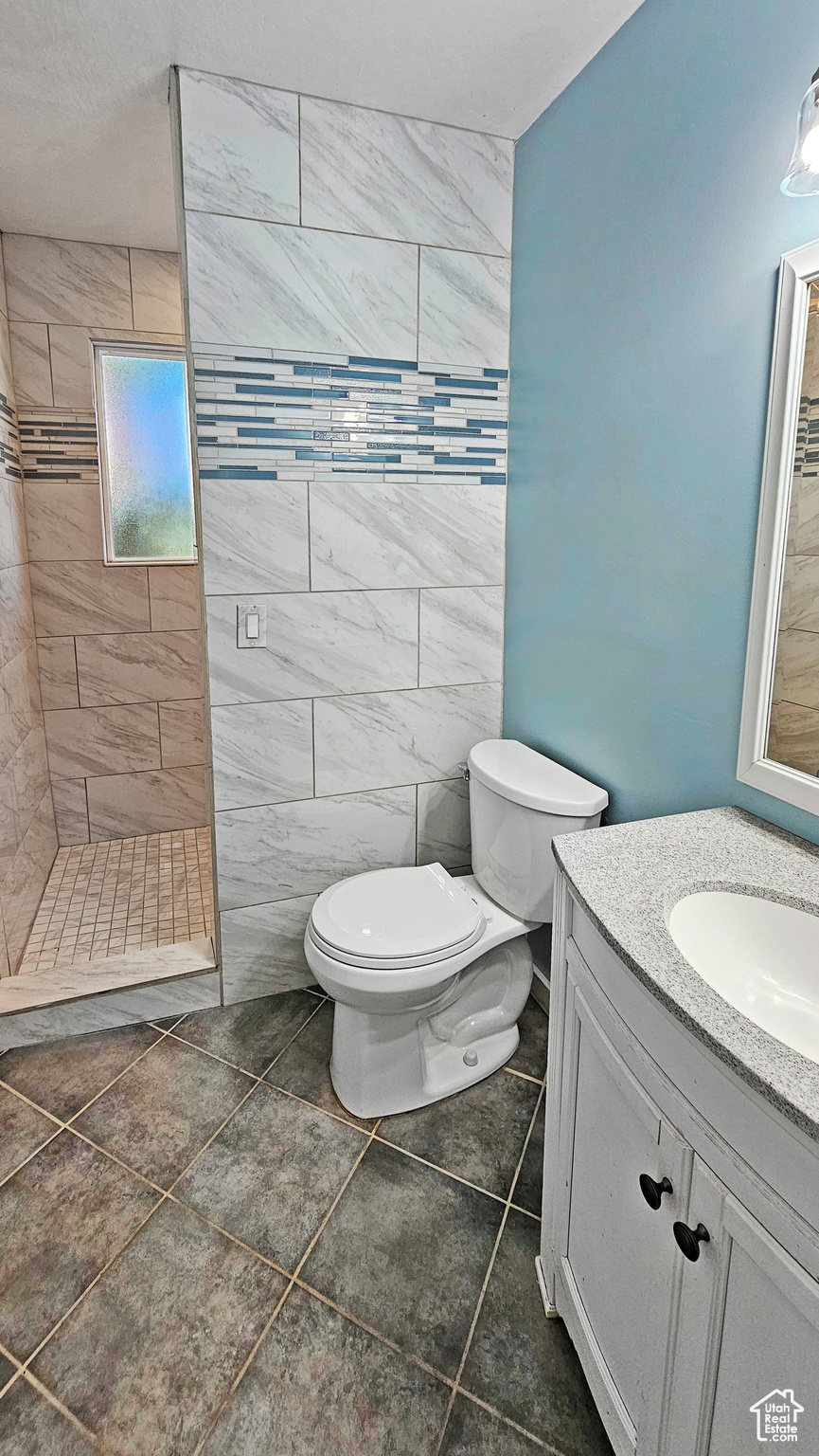 Bathroom with tile walls, tile patterned floors, tiled shower, vanity, and toilet