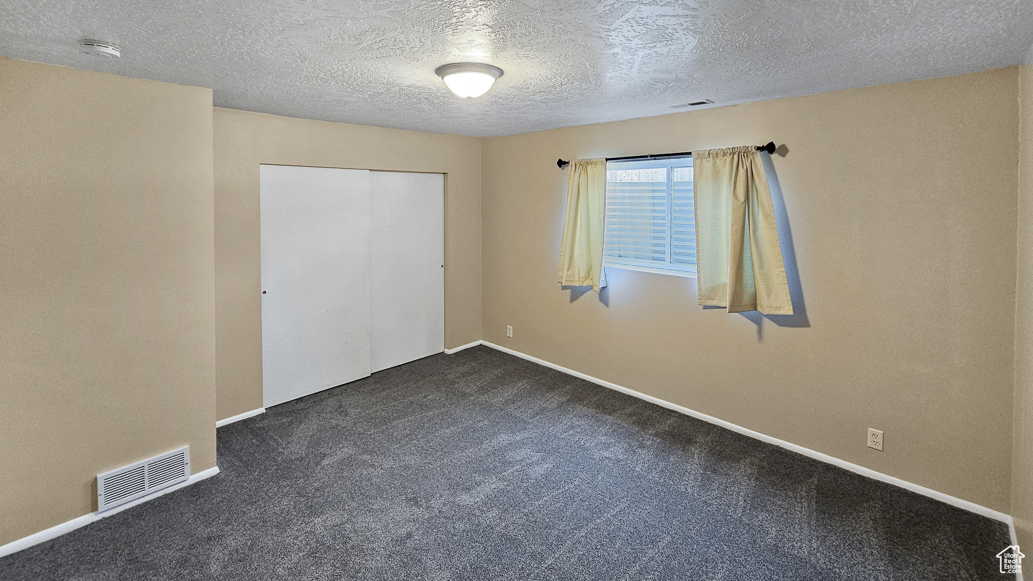 Unfurnished bedroom with a textured ceiling, a closet, and dark colored carpet