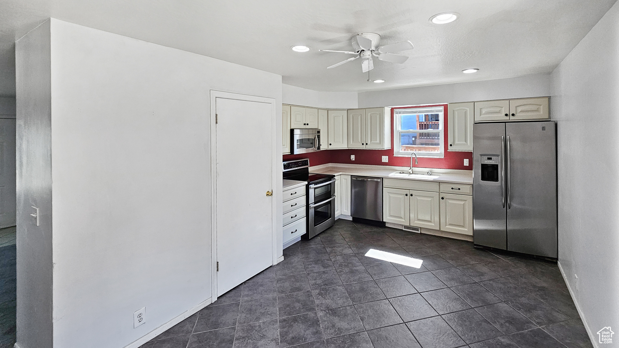 Kitchen with appliances with stainless steel finishes, sink, ceiling fan, and dark tile patterned flooring