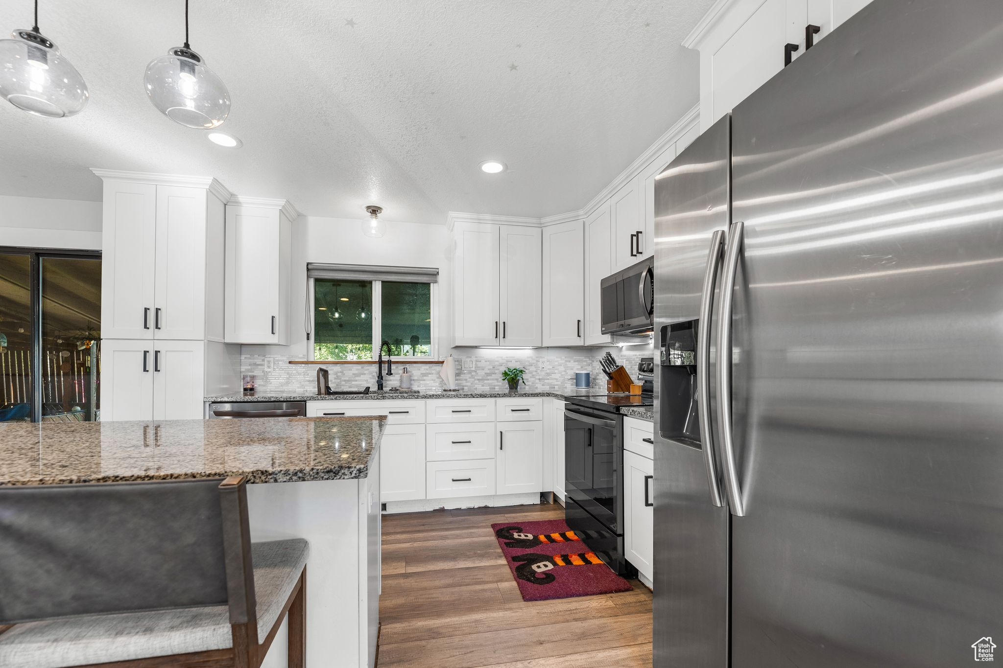 Kitchen with pendant lighting, dark stone counters, dark wood-type flooring, white cabinets, and appliances with stainless steel finishes