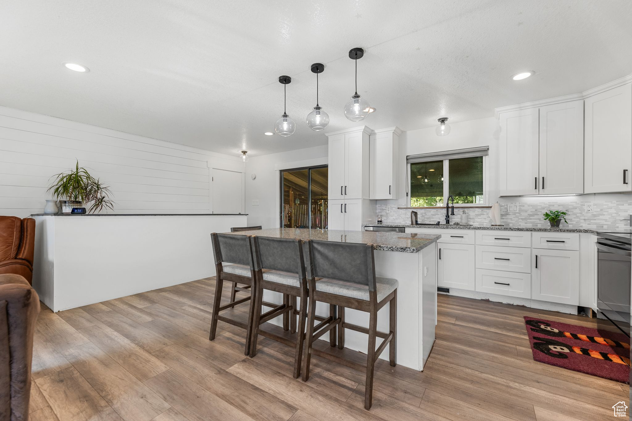 Kitchen with pendant lighting, light hardwood / wood-style flooring, stone counters, white cabinetry, and a center island