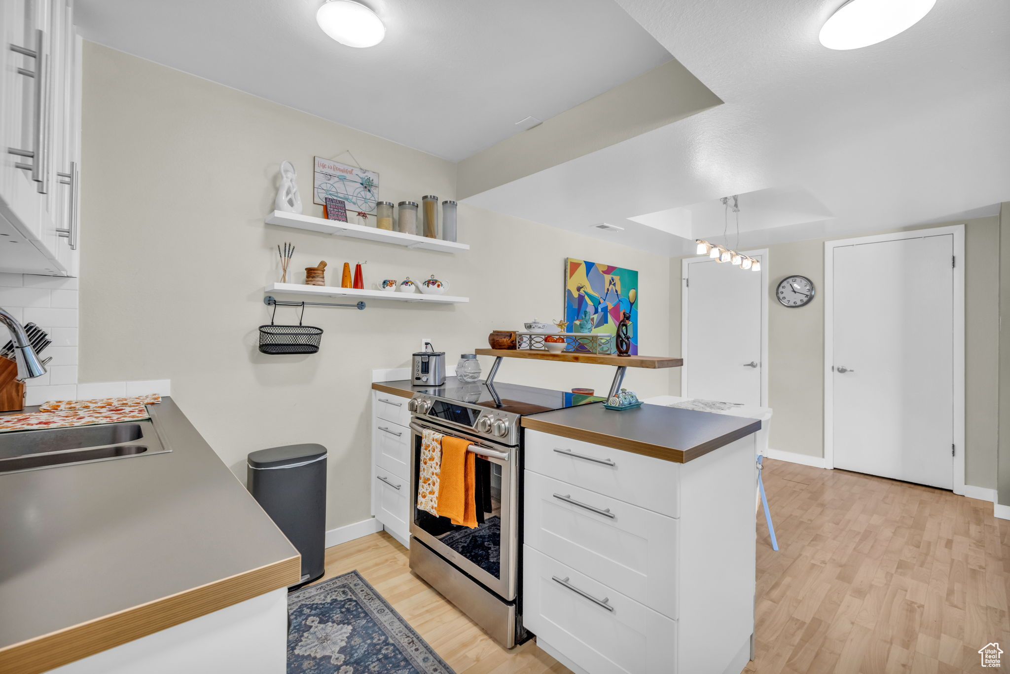 Kitchen featuring light wood-type flooring, sink, white cabinetry, decorative light fixtures, and stainless steel electric range