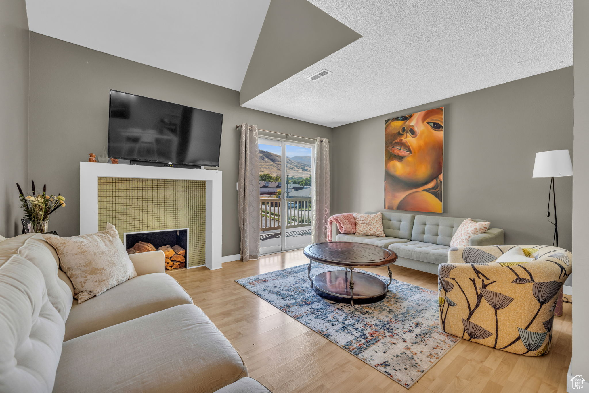 Living room with a tiled fireplace, light hardwood / wood-style floors, and a textured ceiling