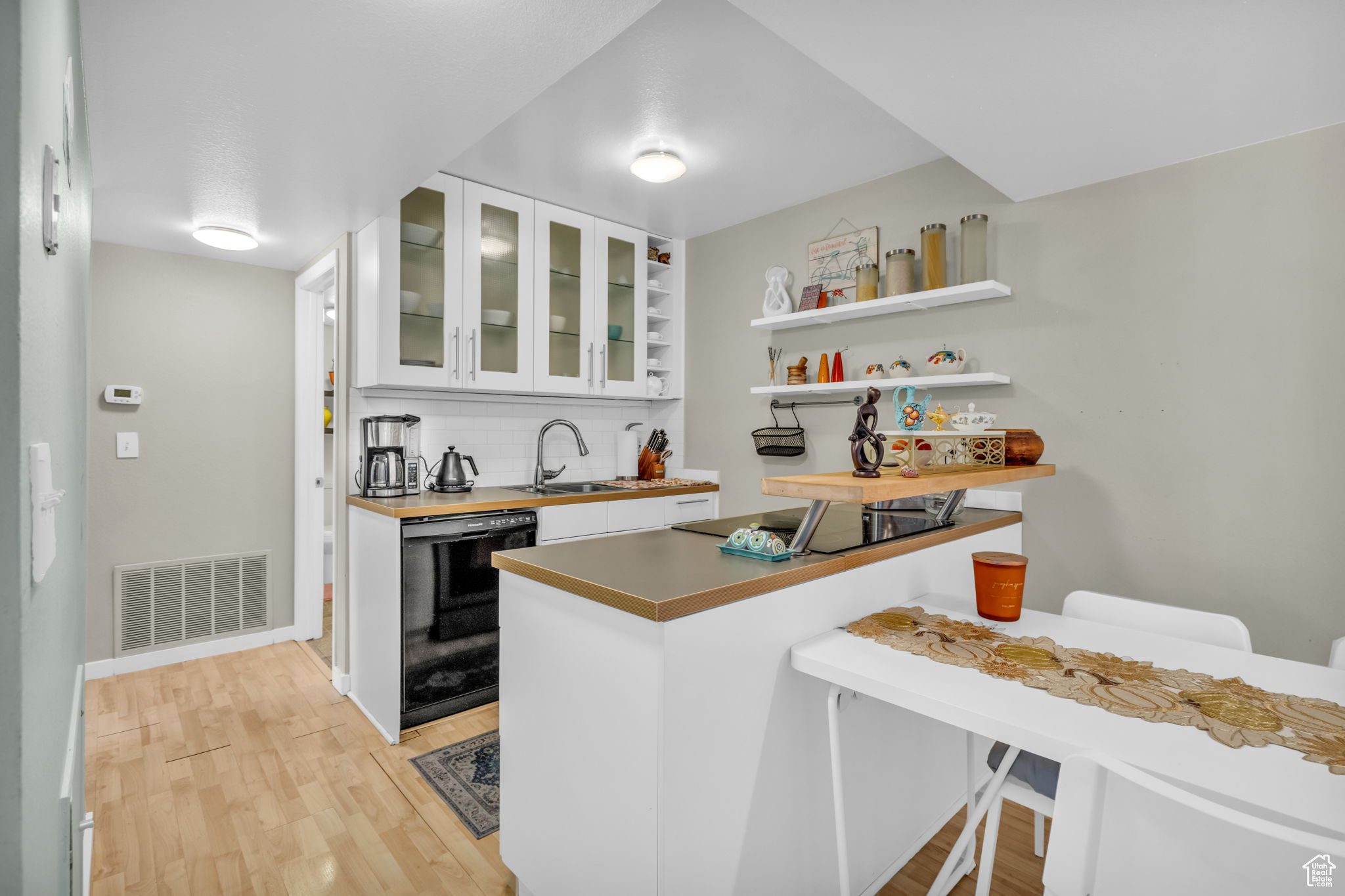 Kitchen with white cabinets, backsplash, kitchen peninsula, light wood-type flooring, and black appliances