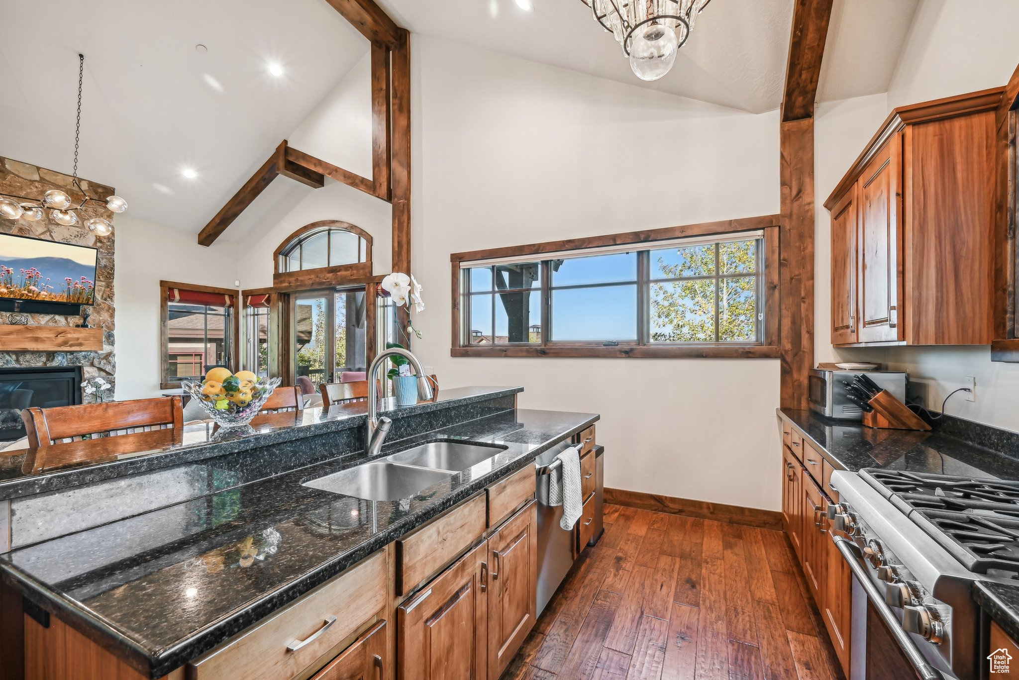 Kitchen with sink, a stone fireplace, decorative light fixtures, dark hardwood / wood-style flooring, and dark stone countertops