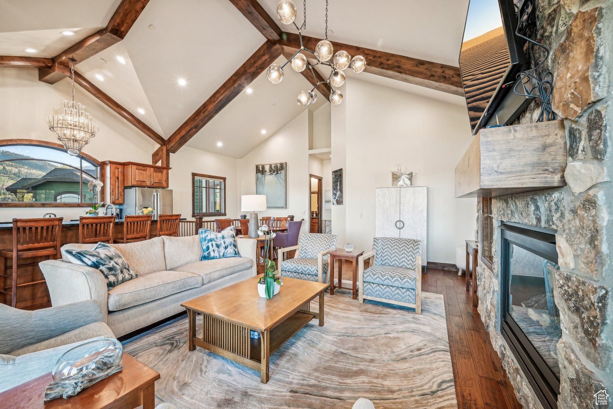 Living room featuring light wood-type flooring, beamed ceiling, a notable chandelier, a fireplace, and high vaulted ceiling