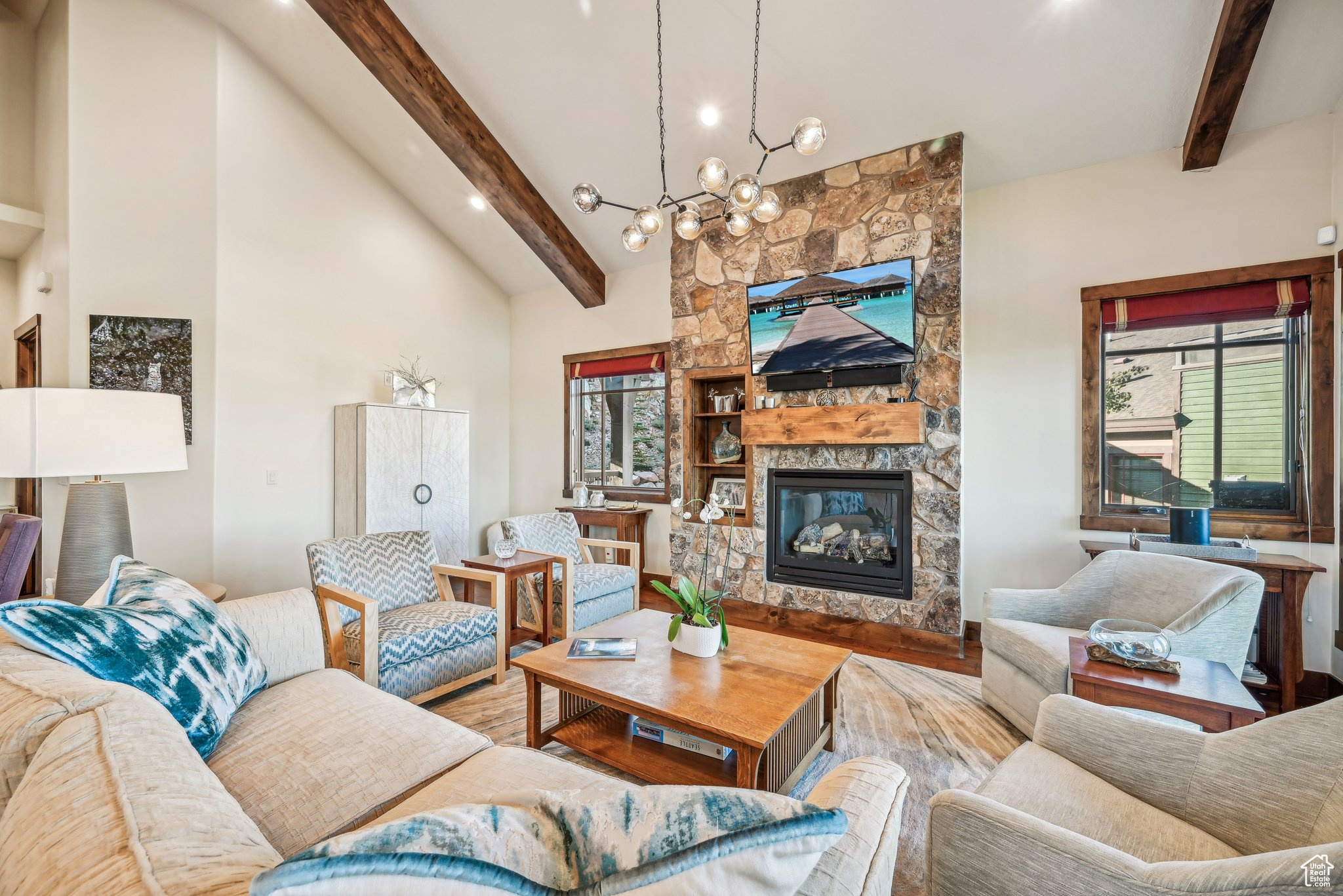 Living room featuring beamed ceiling, an inviting chandelier, high vaulted ceiling, hardwood / wood-style floors, and a stone fireplace