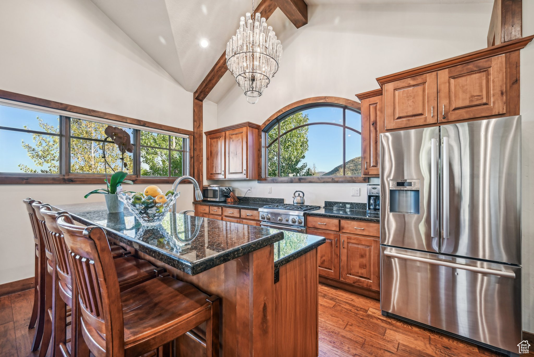 Kitchen with a kitchen island, stainless steel appliances, a notable chandelier, dark stone counters, and dark hardwood / wood-style flooring