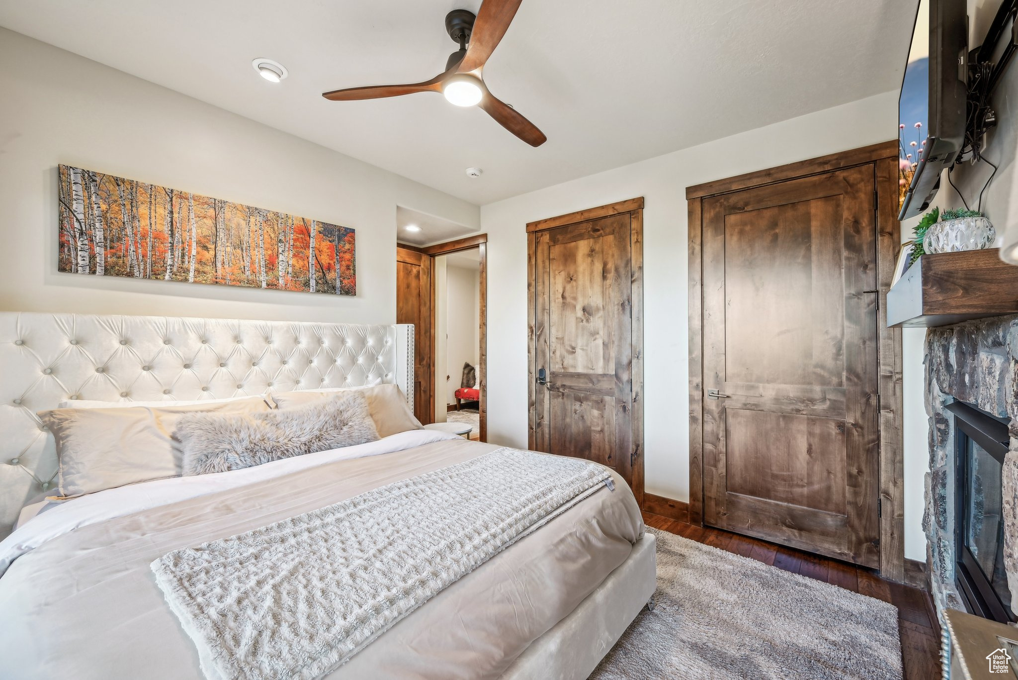 Bedroom featuring wood-type flooring, a stone fireplace, two closets, and ceiling fan