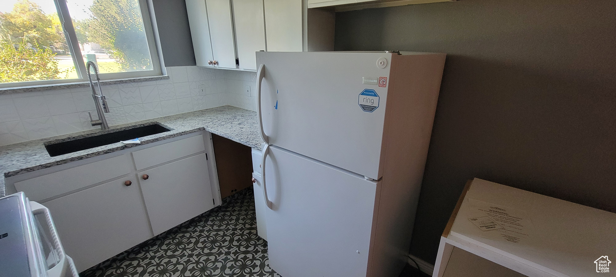 Kitchen with light stone counters, white cabinets, tasteful backsplash, white fridge, and sink