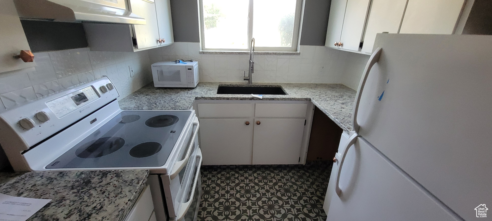 Kitchen with tasteful backsplash, sink, white cabinetry, white appliances, and light stone countertops