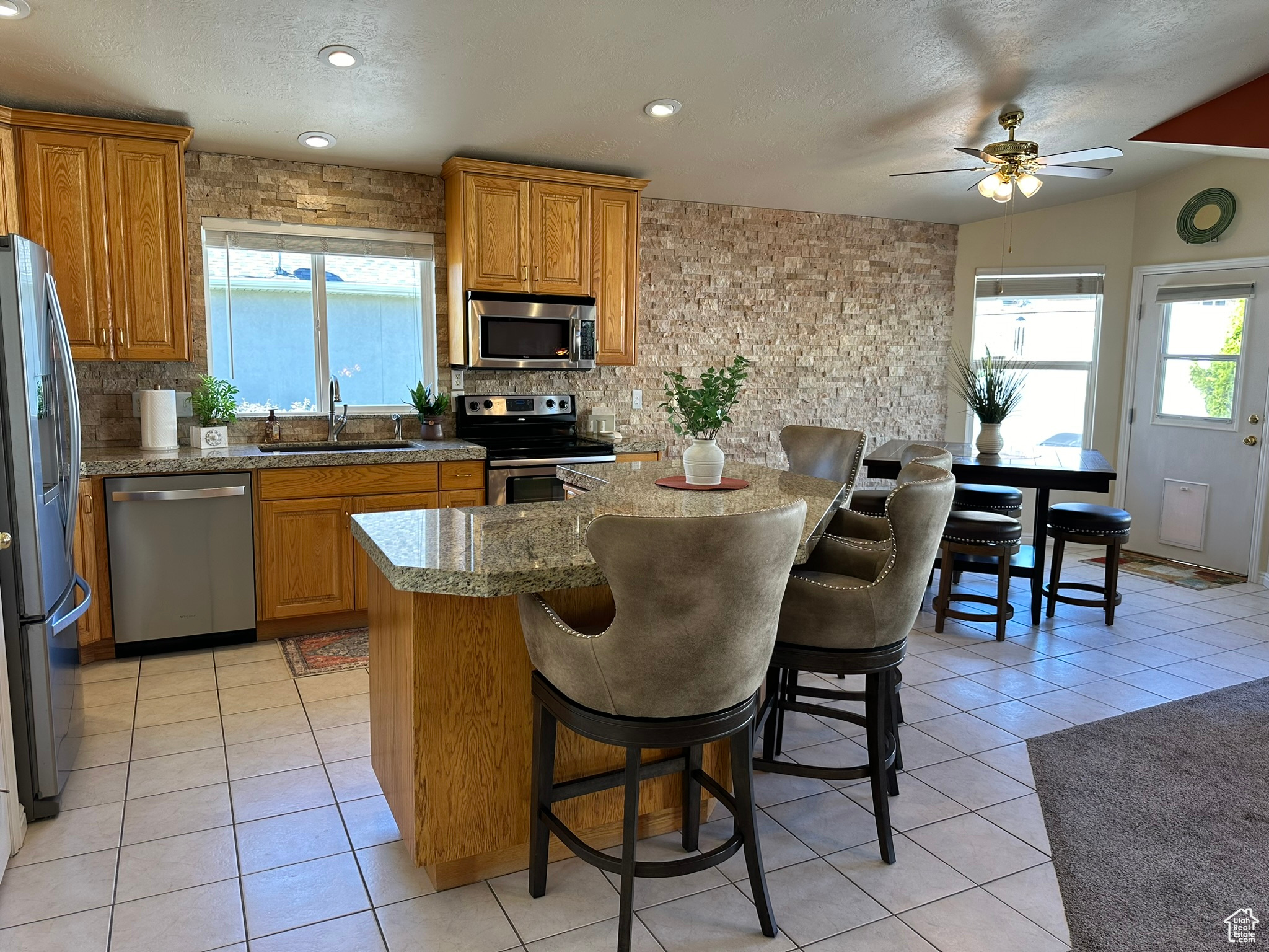 Kitchen with a breakfast bar, sink, stainless steel appliances, light tile patterned floors, and ceiling fan