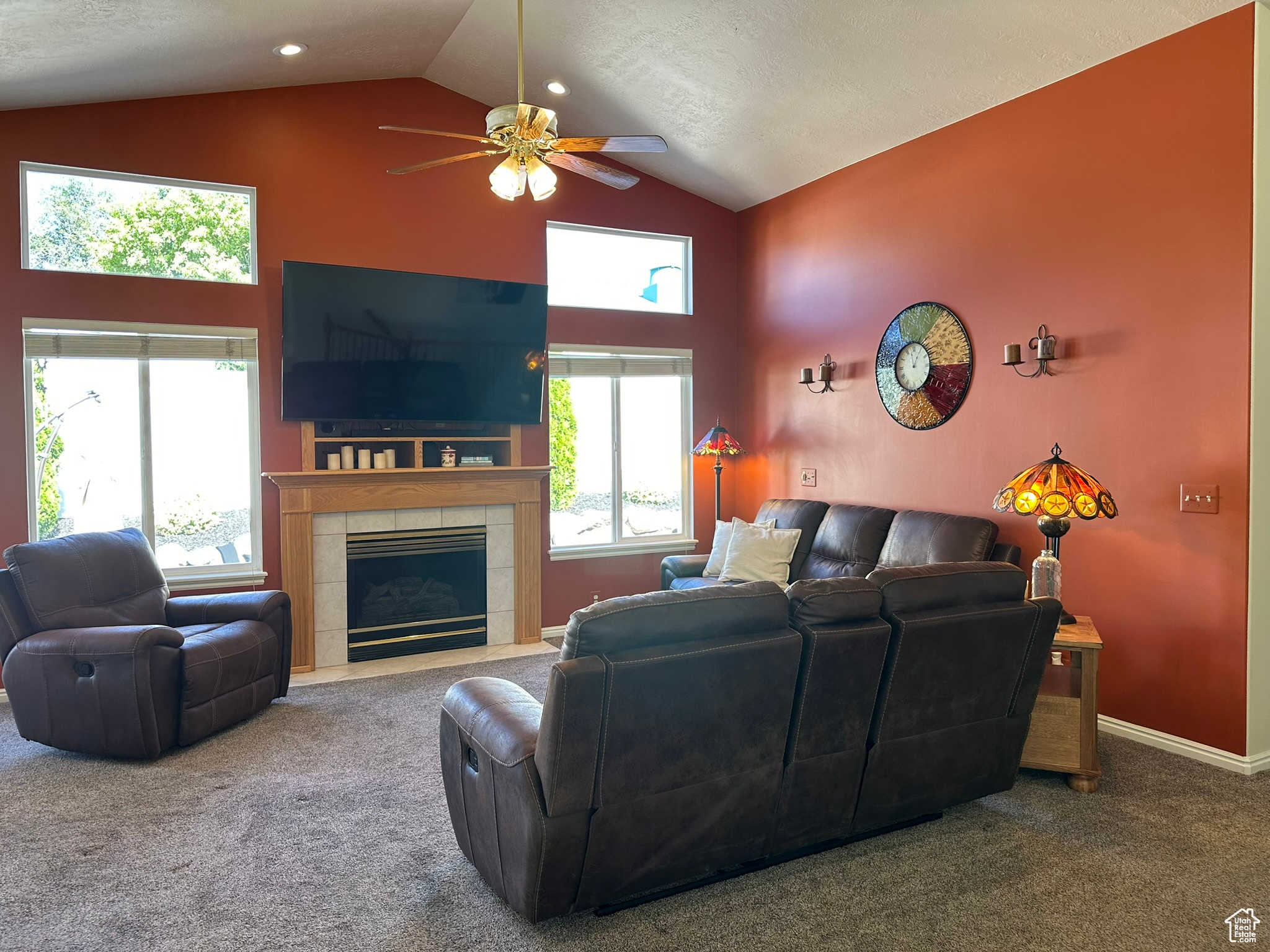 Carpeted living room featuring ceiling fan, a textured ceiling, a tiled fireplace, and high vaulted ceiling