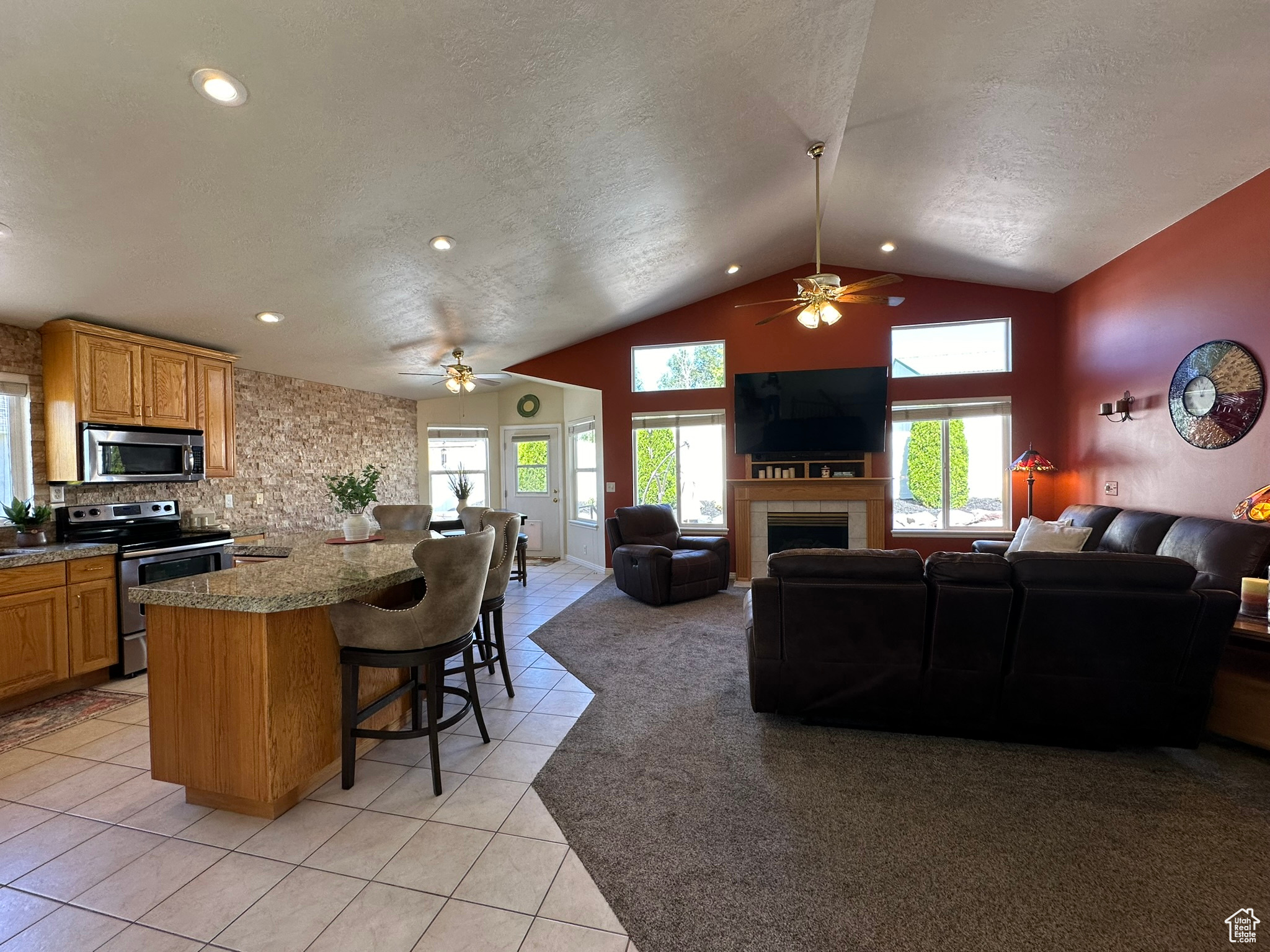 Kitchen featuring a breakfast bar area, a tiled fireplace, vaulted ceiling, stainless steel appliances, and ceiling fan