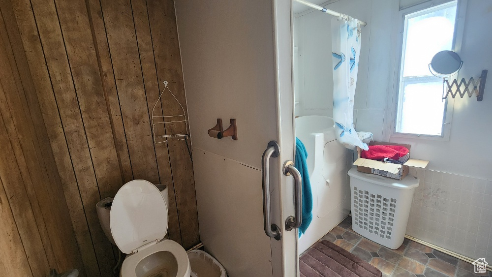 Bathroom with wooden walls, toilet, and a shower with curtain