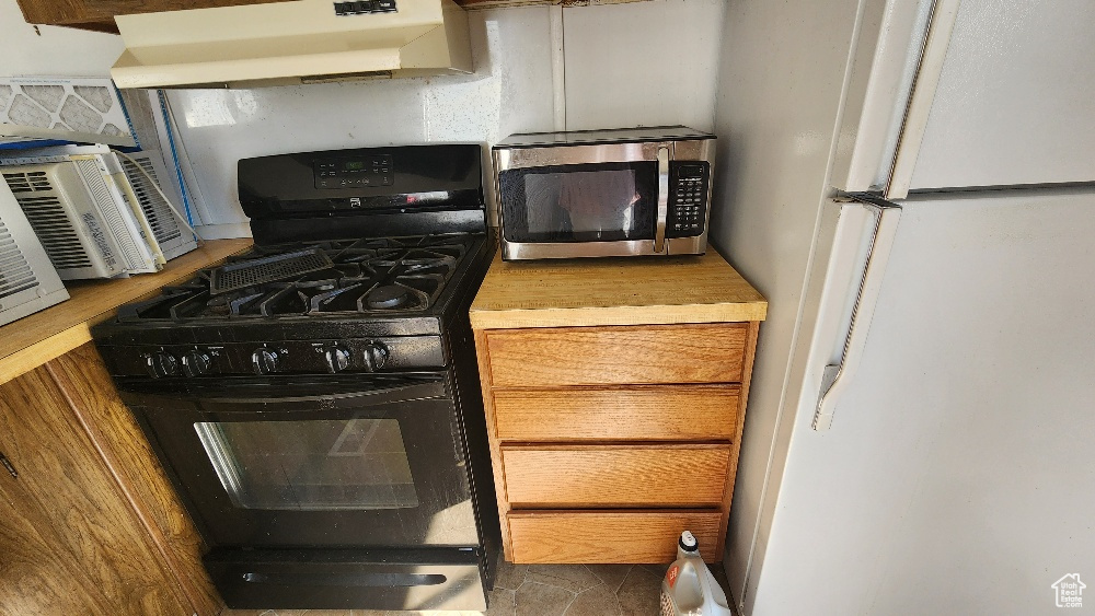 Kitchen with ventilation hood, white refrigerator, and black gas range