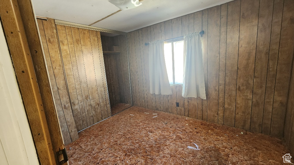 Unfurnished room featuring wood walls and carpet