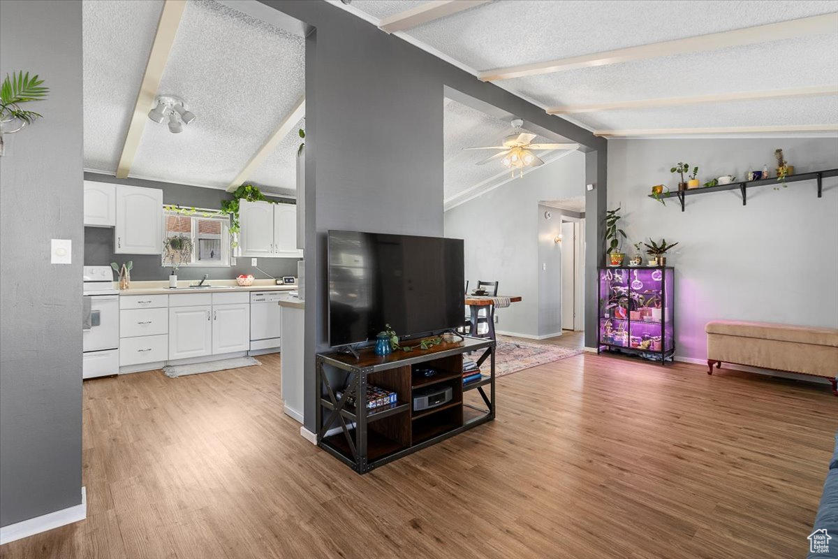 Living room featuring vaulted ceiling with beams, ceiling fan, hardwood / wood-style floors, and a textured ceiling