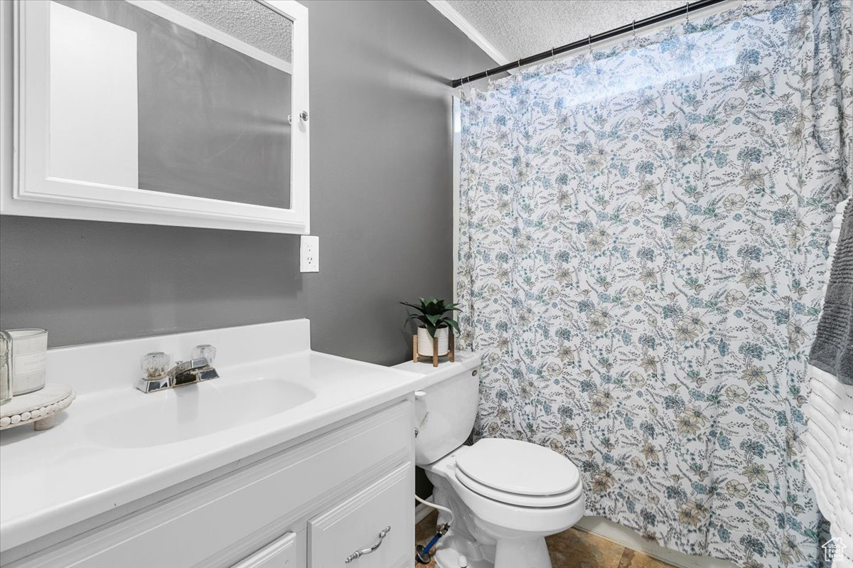 Bathroom featuring a textured ceiling, curtained shower, vanity, and toilet