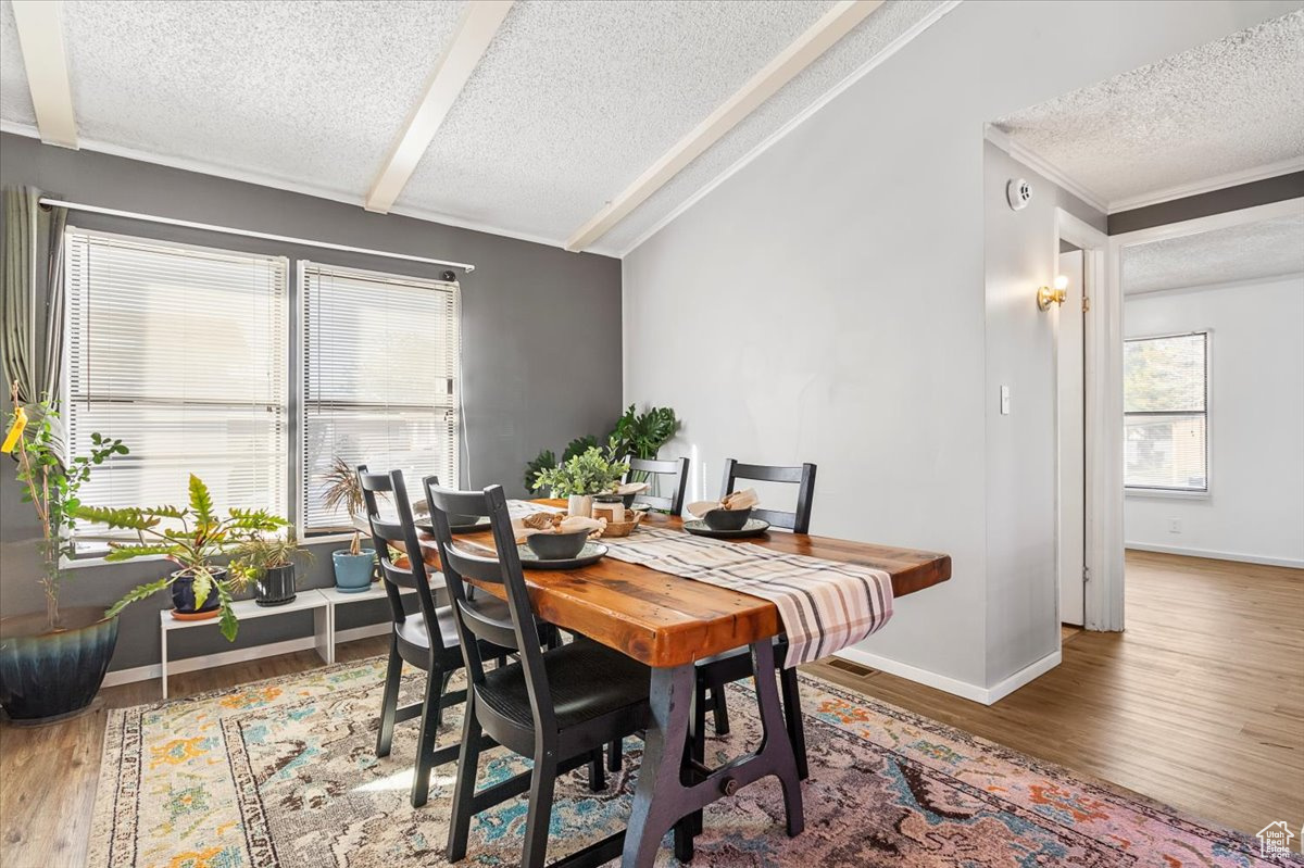 Dining space with a textured ceiling, wood-type flooring, and lofted ceiling with beams