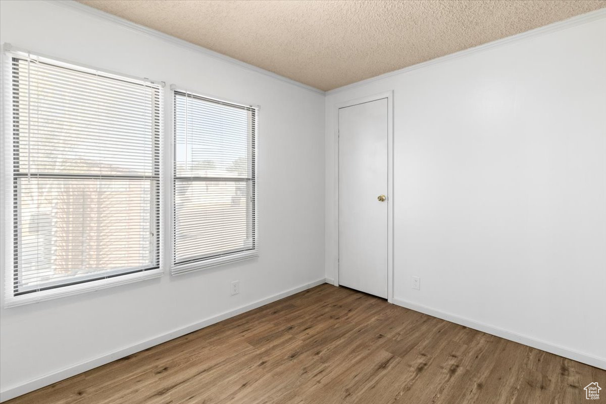 Unfurnished room featuring a textured ceiling, ornamental molding, and hardwood / wood-style flooring