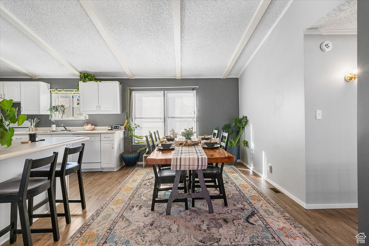 Dining space with beam ceiling, light hardwood / wood-style floors, sink, and a textured ceiling