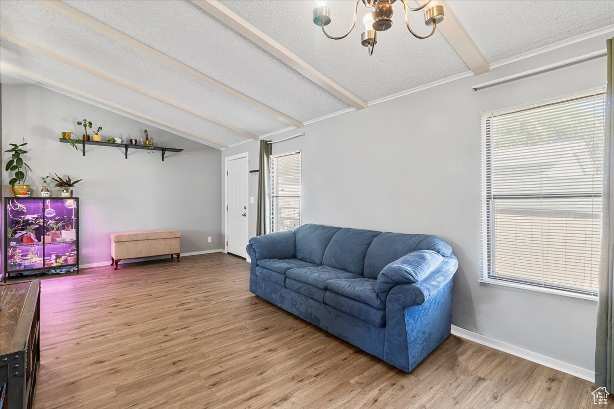 Living room featuring wood-type flooring, an inviting chandelier, lofted ceiling with beams, and a textured ceiling