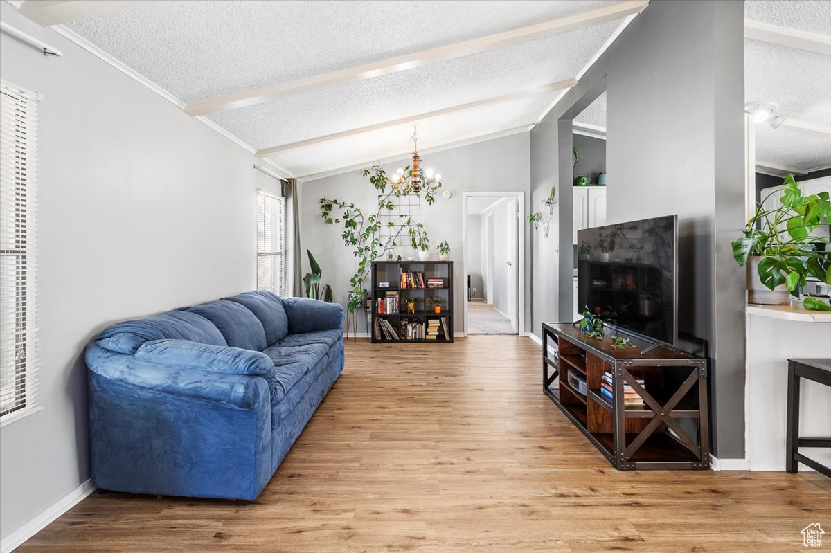 Living room with an inviting chandelier, a textured ceiling, light hardwood / wood-style flooring, and lofted ceiling with beams