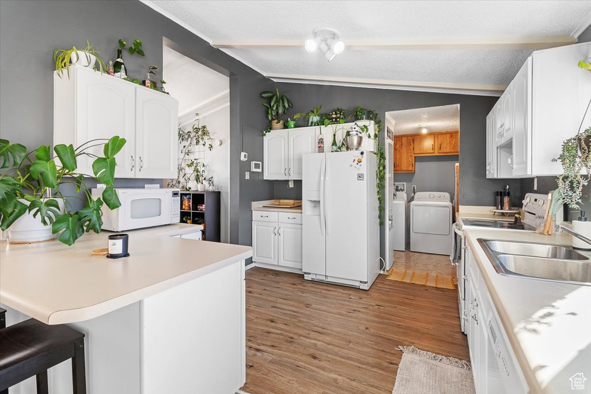 Kitchen with light hardwood / wood-style floors, a breakfast bar area, white cabinets, lofted ceiling, and white appliances