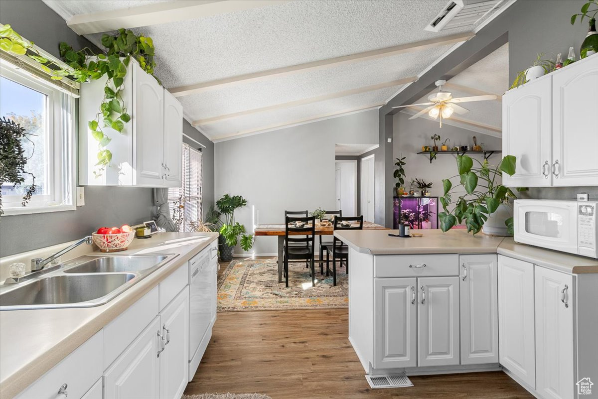 Kitchen with white cabinets, white appliances, ceiling fan, hardwood / wood-style flooring, and vaulted ceiling with beams