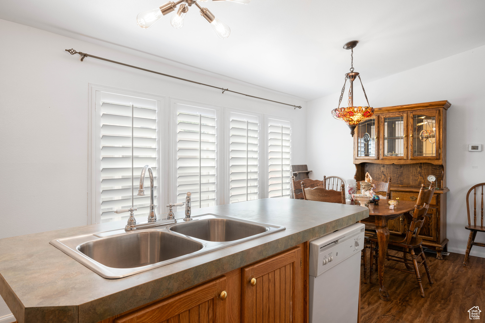 Kitchen with dark wood-type flooring, sink, an island with sink, decorative light fixtures, and white dishwasher