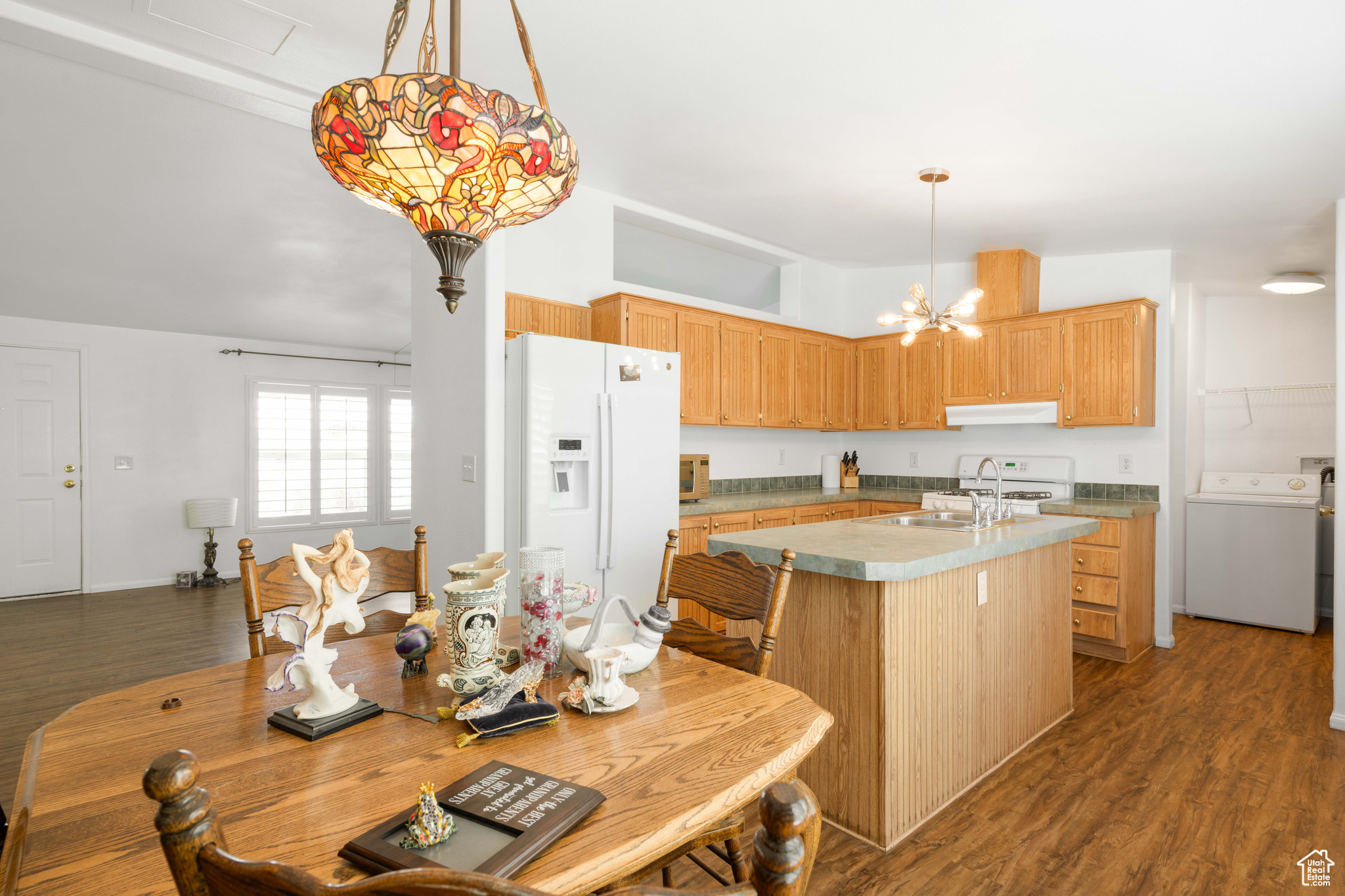 Kitchen with pendant lighting, white appliances, washer / clothes dryer, dark hardwood / wood-style floors, and a notable chandelier