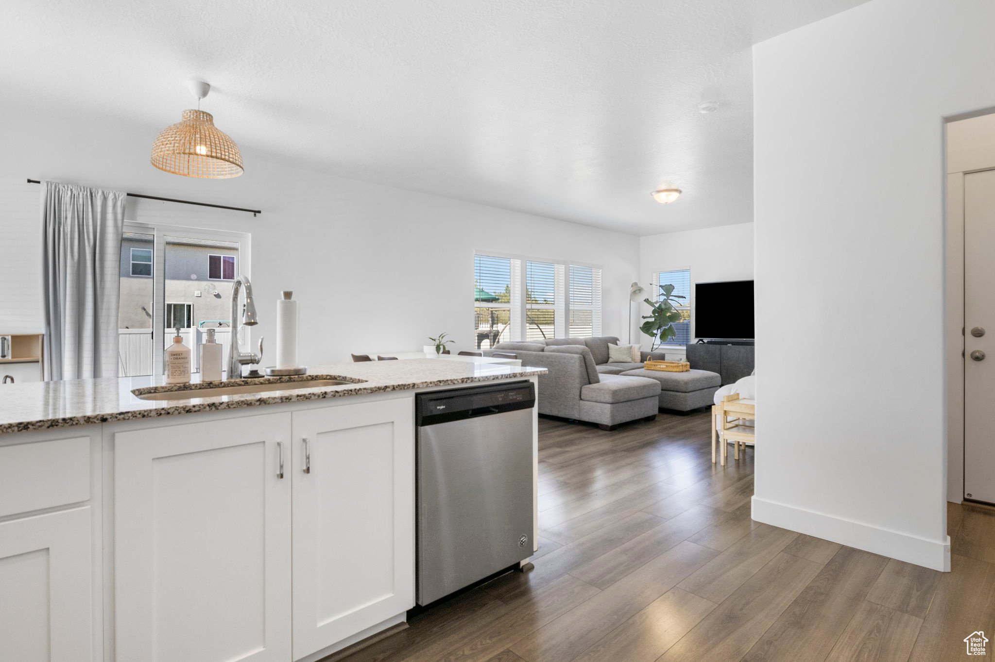 Kitchen featuring white cabinets, dishwasher, light stone countertops, dark hardwood / wood-style floors, and sink