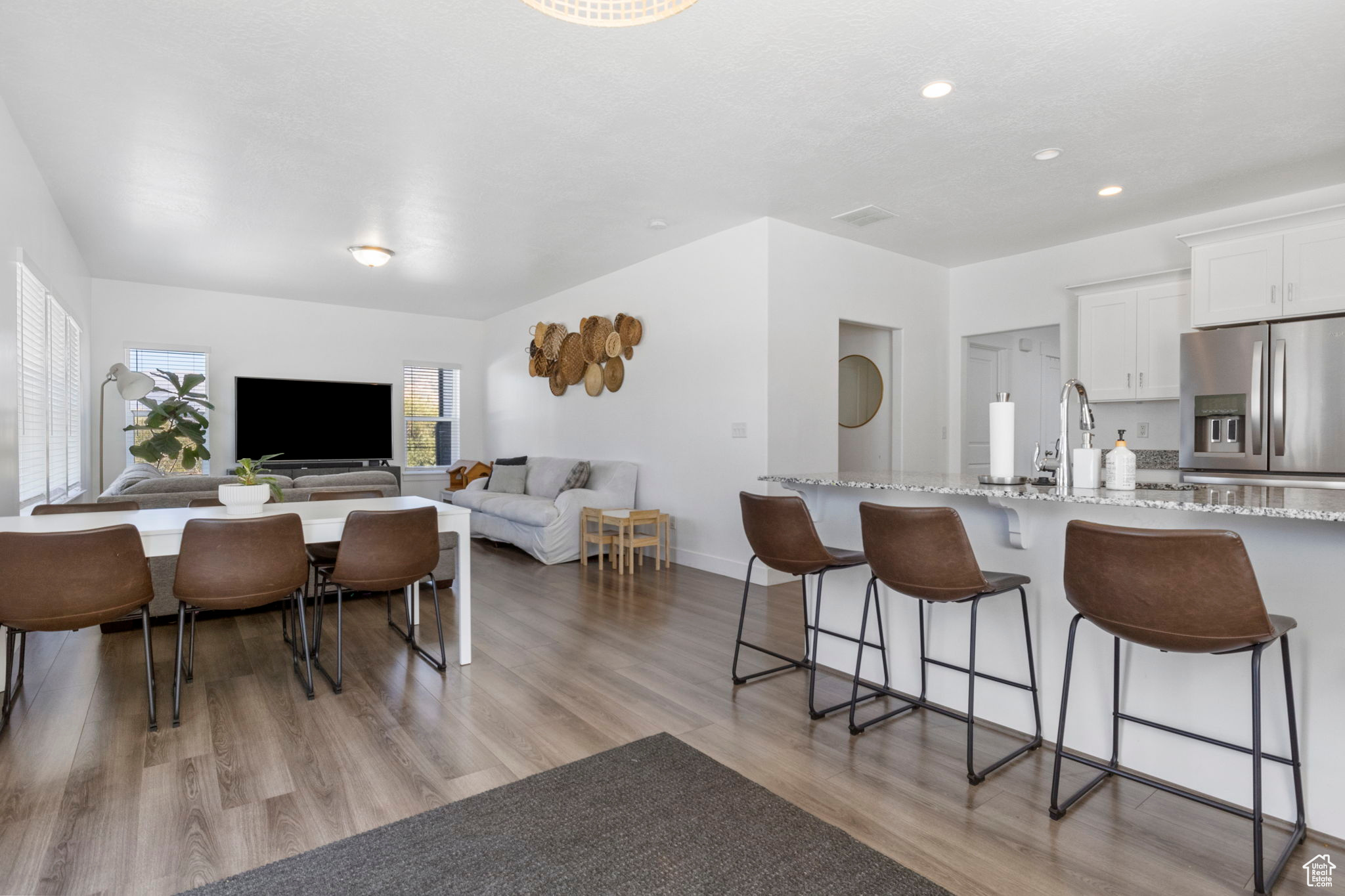 Kitchen featuring a kitchen breakfast bar, light hardwood / wood-style floors, white cabinets, light stone countertops, and stainless steel fridge with ice dispenser