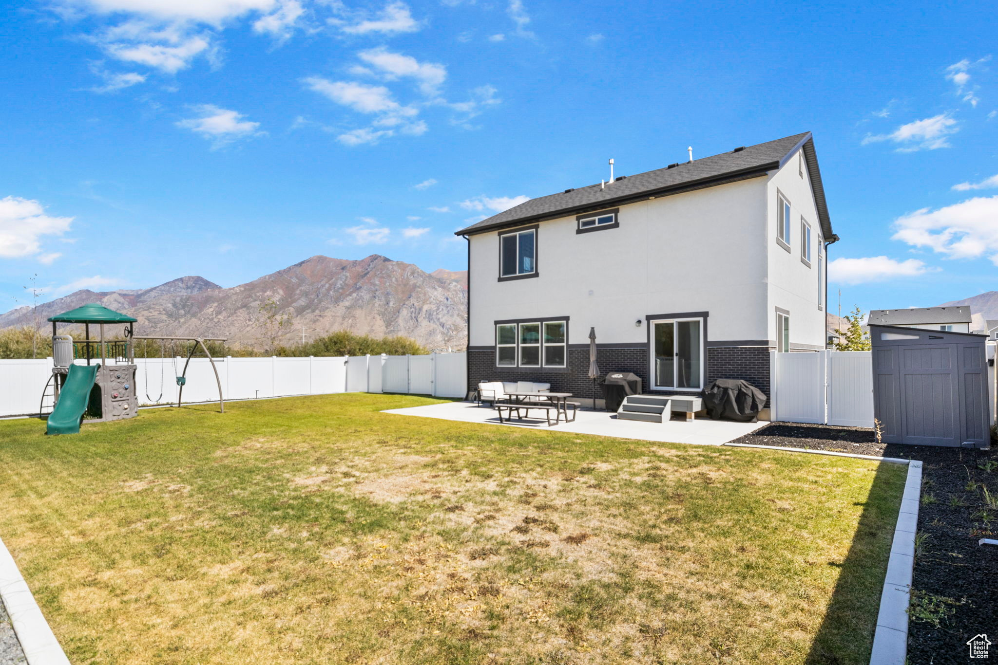 Back of house featuring a playground, a mountain view, a lawn, and a patio area