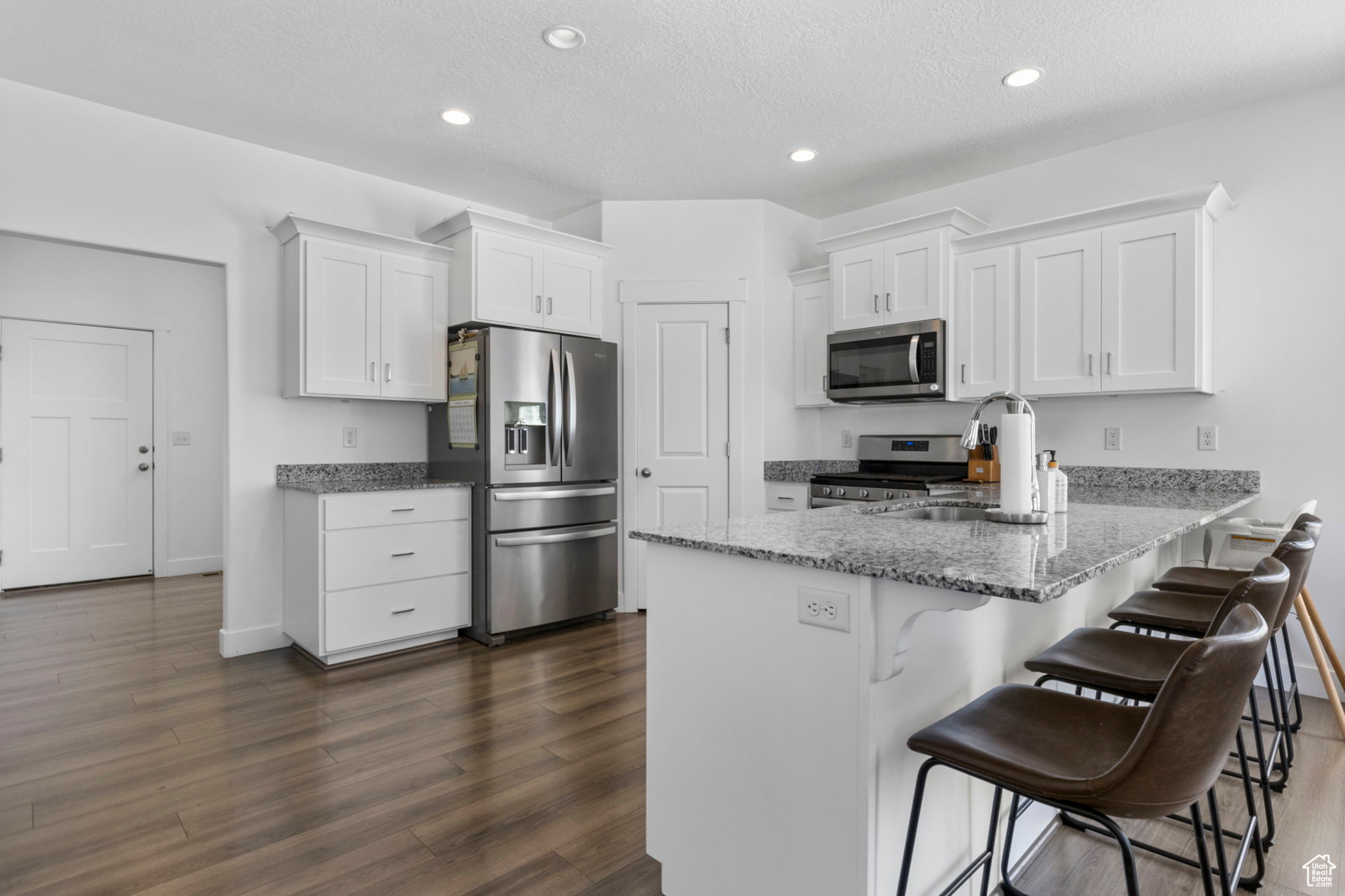 Kitchen with stainless steel appliances, white cabinetry, kitchen peninsula, and dark wood-type flooring