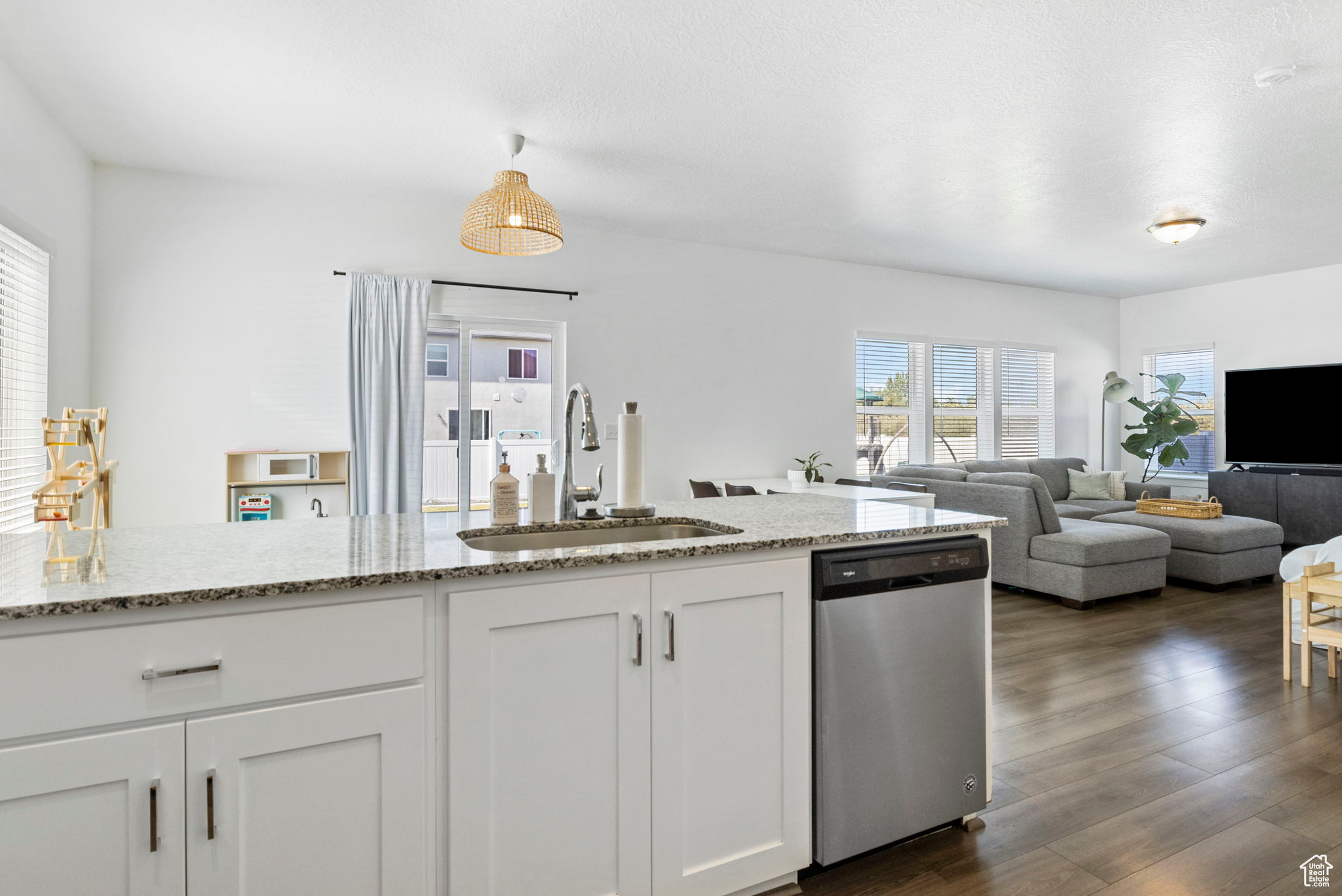 Kitchen with light stone counters, white cabinets, stainless steel dishwasher, dark hardwood / wood-style floors, and sink