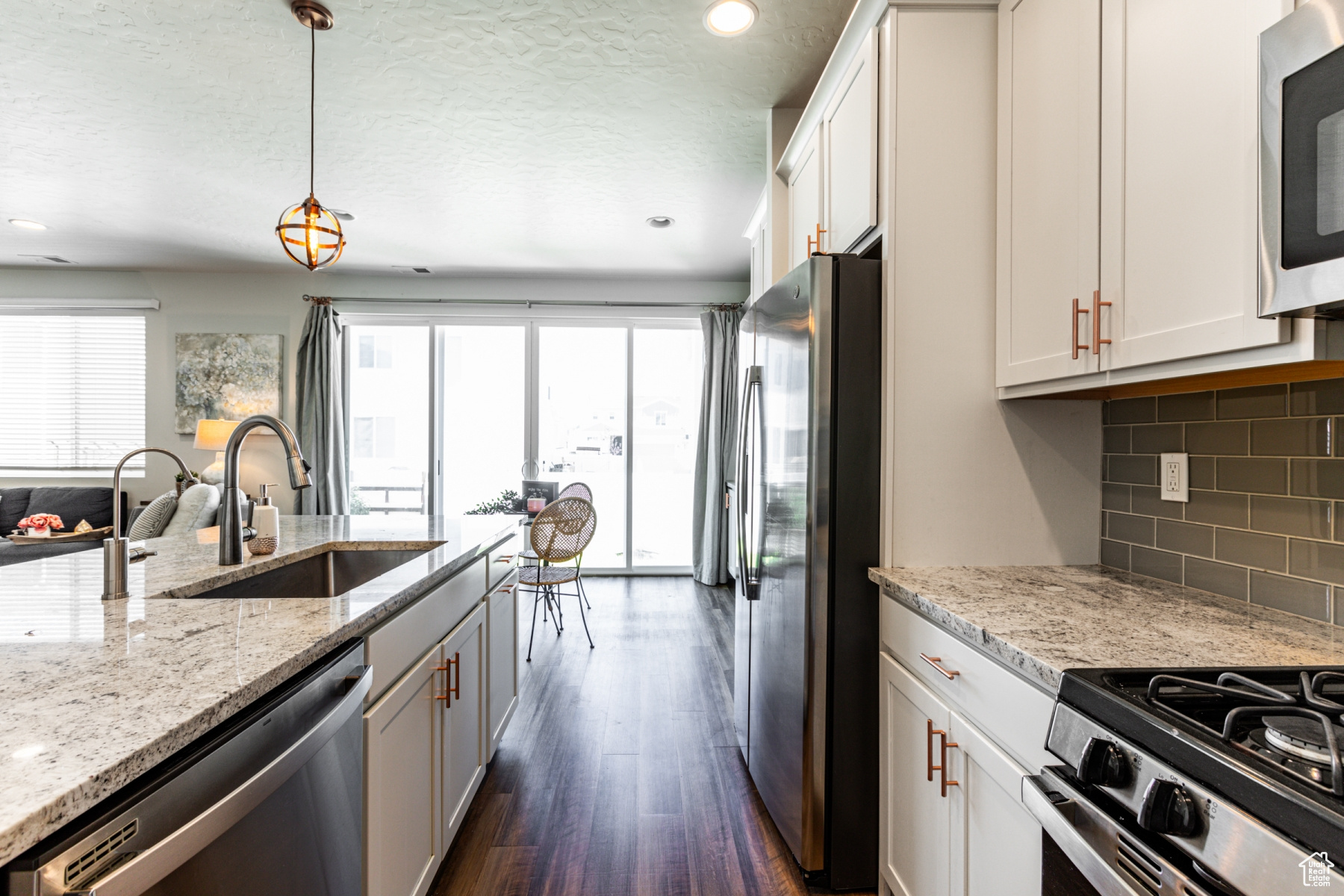 Kitchen with white cabinets, hanging light fixtures, sink, appliances with stainless steel finishes, and dark hardwood / wood-style floors