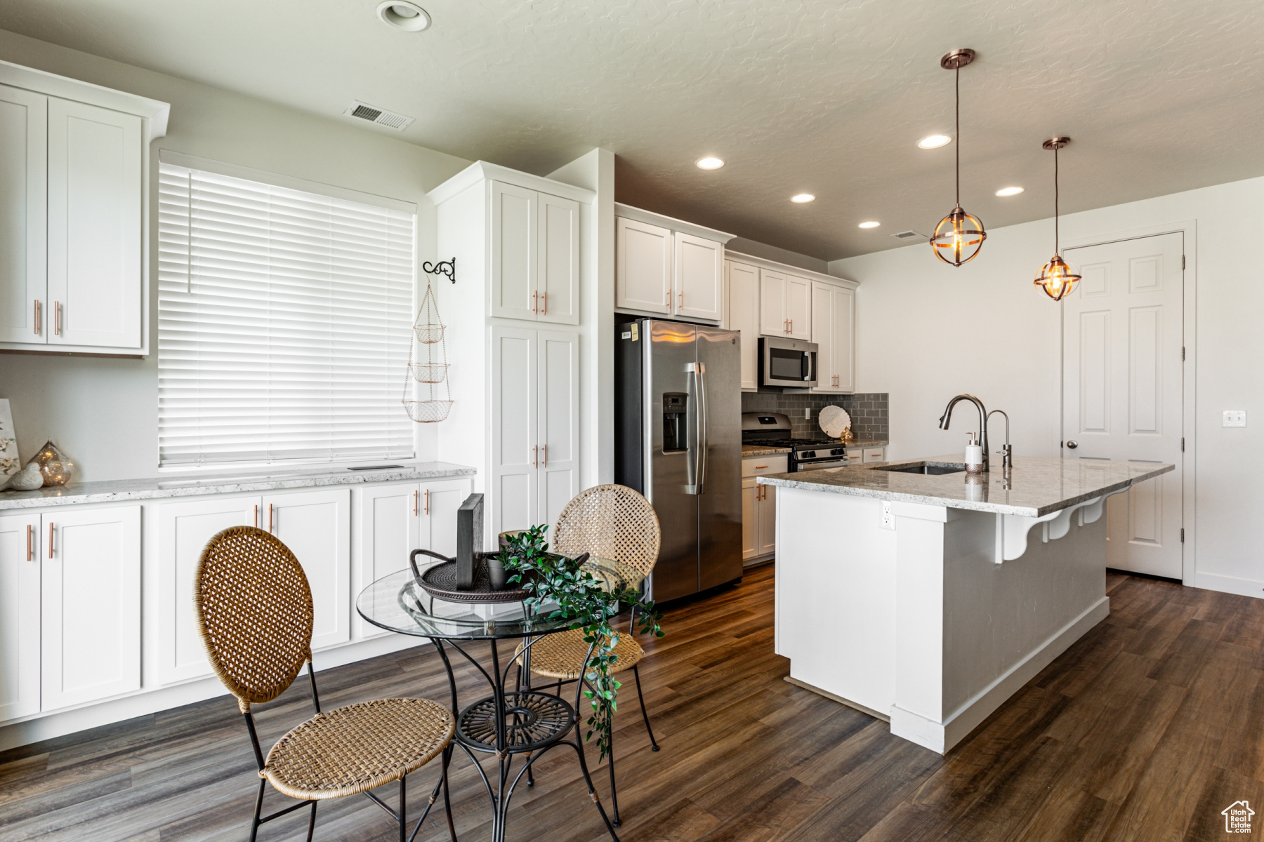 Kitchen featuring light stone counters, a kitchen island with sink, sink, stainless steel appliances, and decorative light fixtures