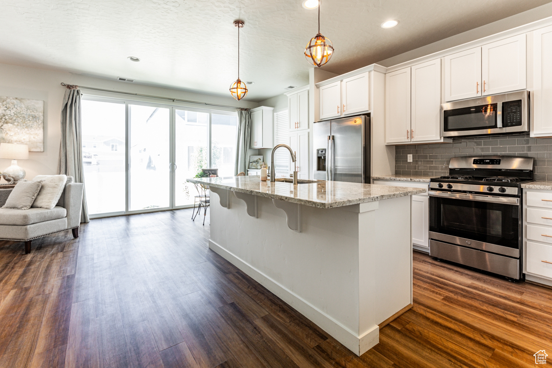 Kitchen with dark hardwood / wood-style floors, a kitchen island with sink, white cabinetry, stainless steel appliances, and decorative light fixtures