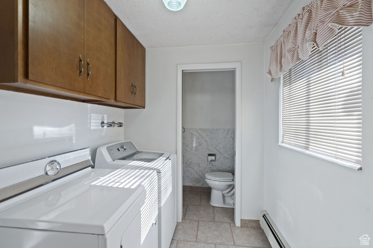 Clothes washing area featuring tile walls, a baseboard heating unit, a textured ceiling, washing machine and clothes dryer, and light tile patterned floors