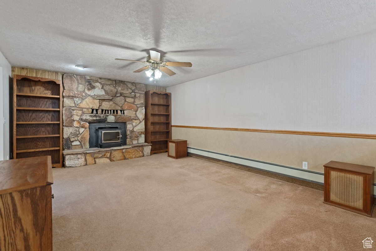 Unfurnished living room featuring ceiling fan, a textured ceiling, a baseboard heating unit, carpet, and a fireplace