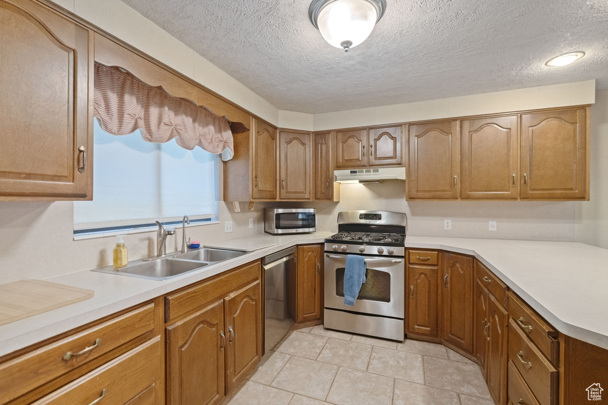 Kitchen featuring stainless steel appliances, a textured ceiling, light tile patterned floors, and sink