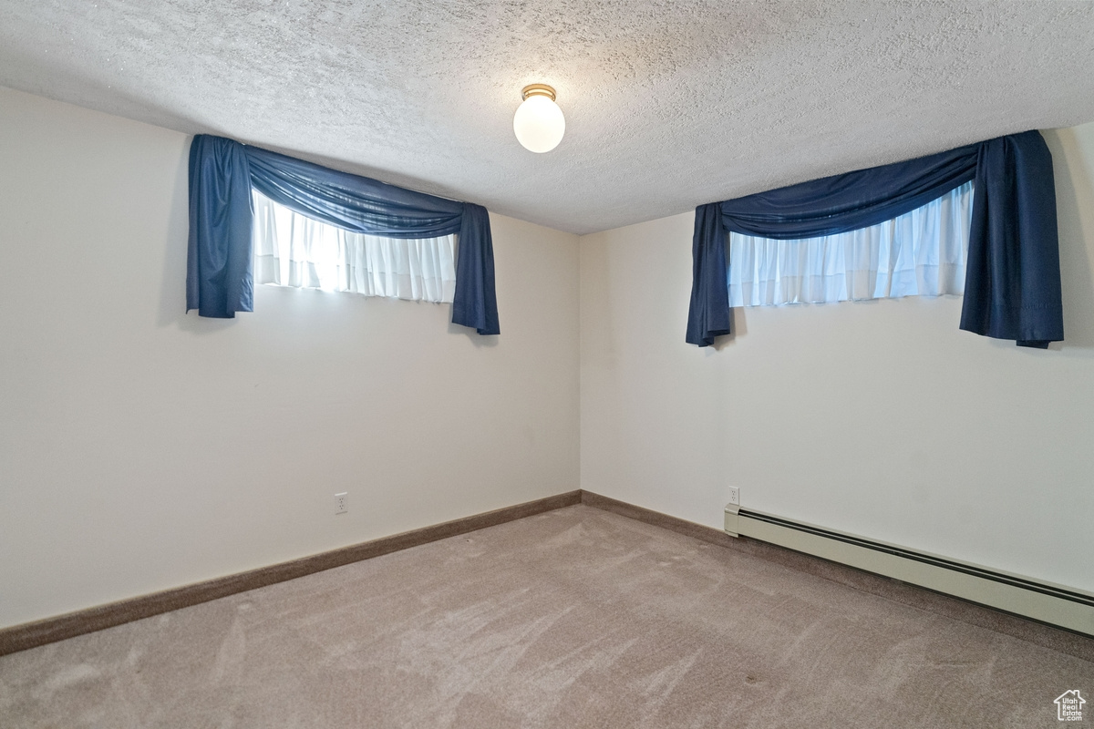 Unfurnished room with a textured ceiling, carpet, and a baseboard radiator